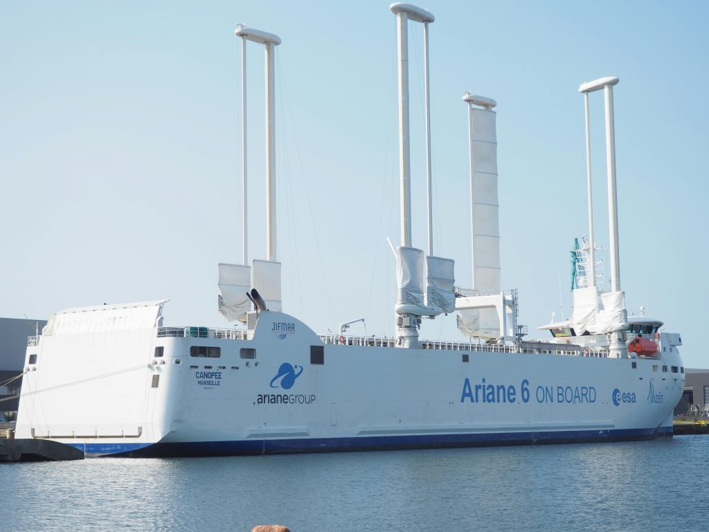 Ariane 6 cargo ship with high-tech sails docked at port during the day.